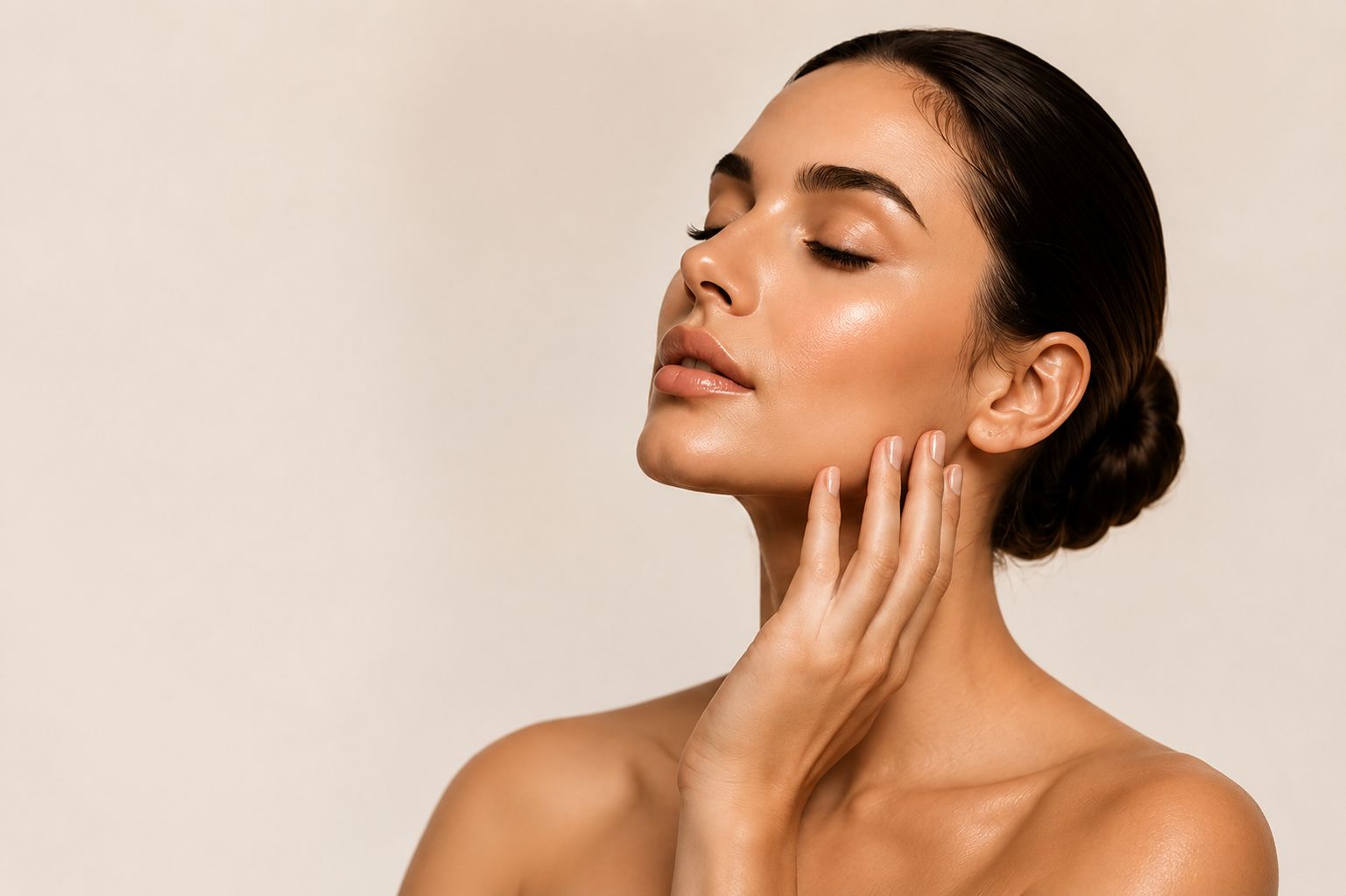 A woman with sleek hair, eyes closed, resting her hands on her neck — radiant, glowing skin